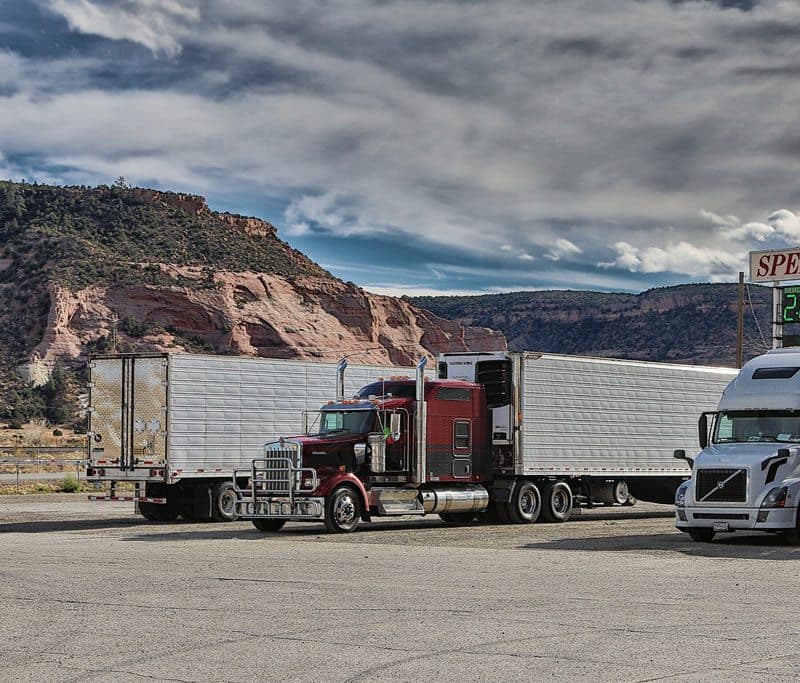 Semi trucks with dry van trailers parked below red rock mesas